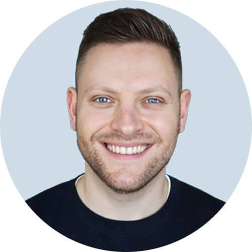 a smiling man with a short beard and blue eyes, wearing a dark sweater, is pictured from the chest up against a light blue background inside a white circle.